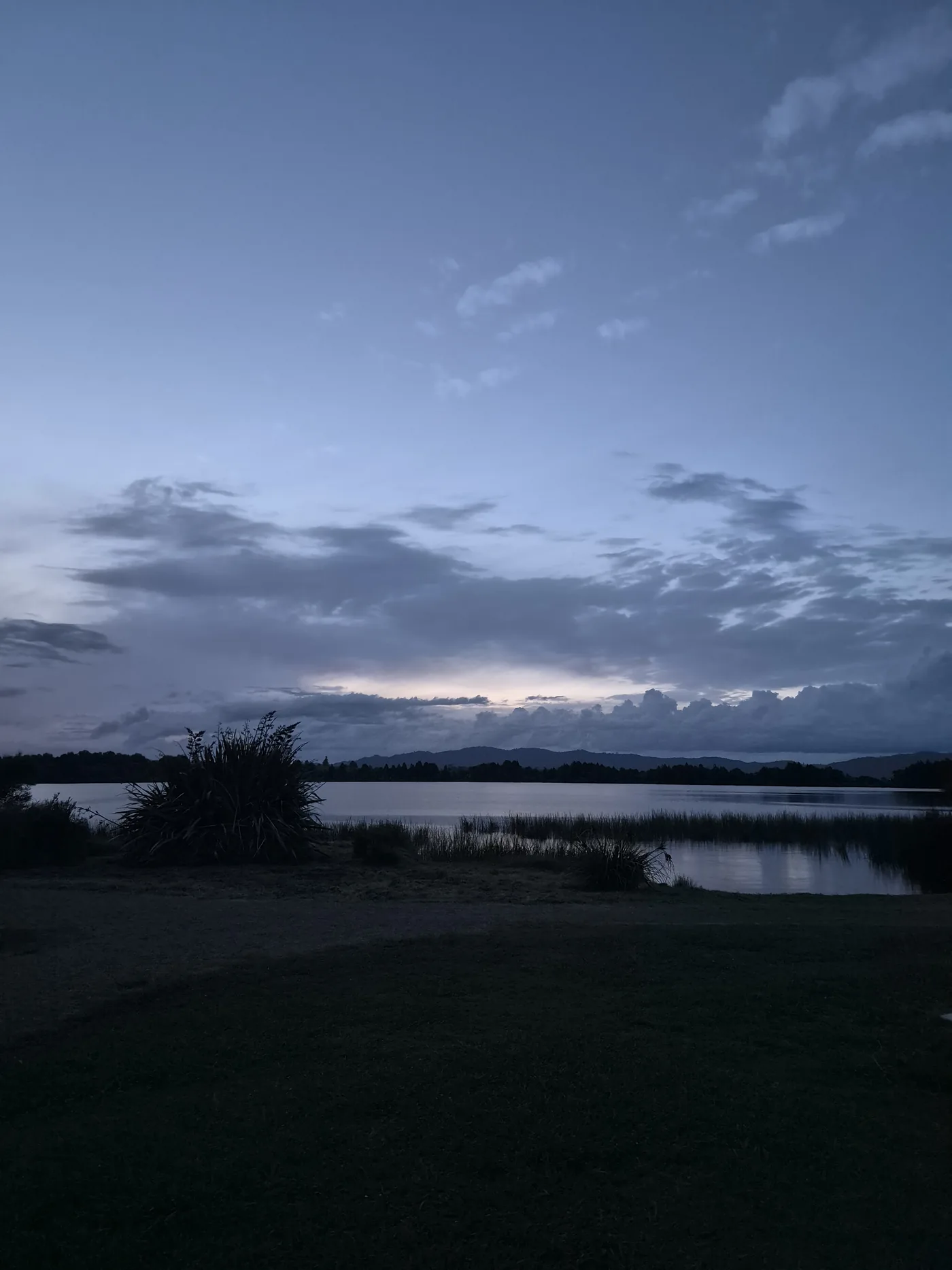 Evening view across Lake Kainui toward the distant Waikato ranges