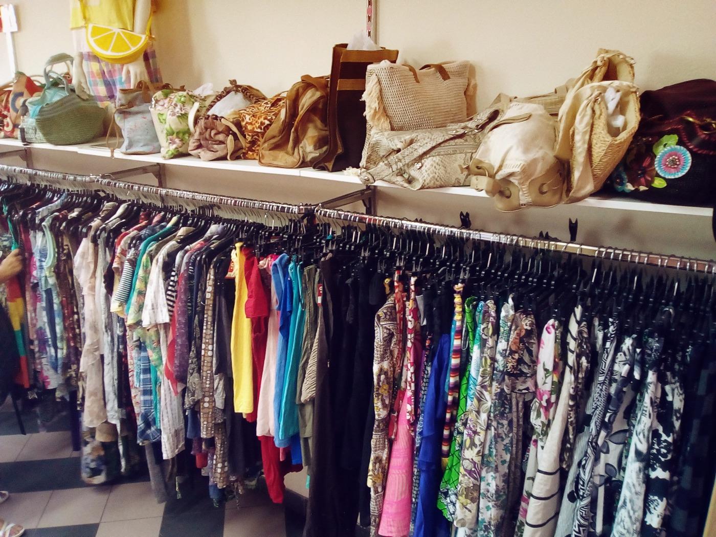 Colourful pre-loved clothing and handbags arranged on shop racks